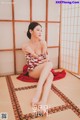 A woman in a red and white kimono sitting on a tatami mat.