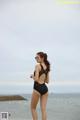 A woman in a black swimsuit standing on the beach.