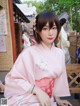 A woman in a pink kimono sitting on a wooden bench.