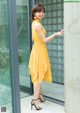 A woman in a yellow dress leaning against a wall.