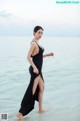 A woman in a black dress standing in the water.