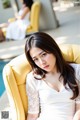 A woman in a white dress sitting on a yellow chair.