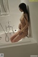 A naked woman sitting in a bathtub in a bathroom.