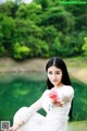 A woman in a white dress holding a pink flower.