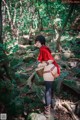 A woman in a red hoodie is standing on a rock in the woods.